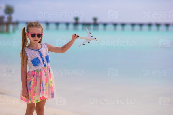 Happy little girl with toy airplane in hands on white sandy beach