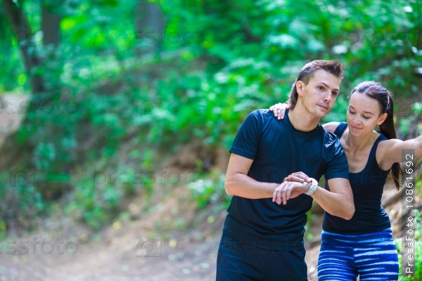 Young active couple looking at smart watch heart rate monitor having break while running at forest