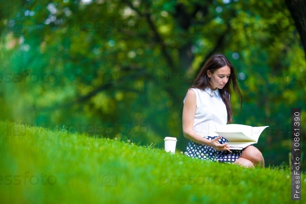 Young woman relaxing with coffee in park reading a book