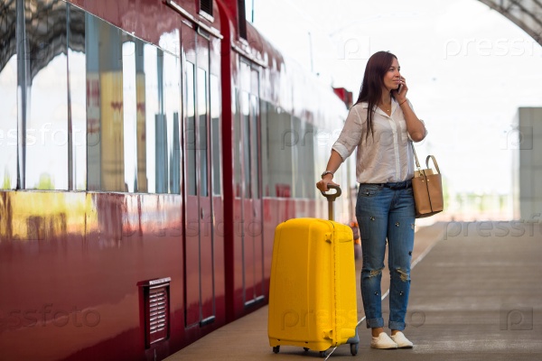 Young woman with luggage talking by cellphone at a train station