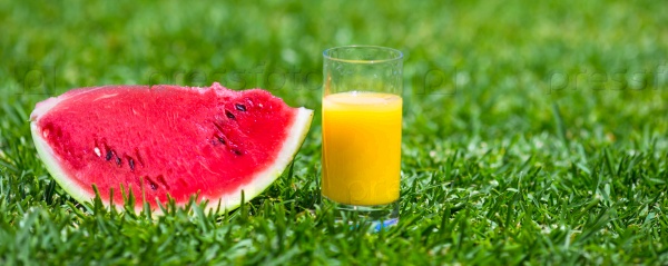 Summer and fresh theme: red ripe slice watermelon and glass of orange juice on green grass