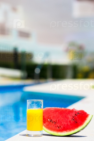 Summer and fresh theme: red ripe slice watermelon and glass of orange juice near pool