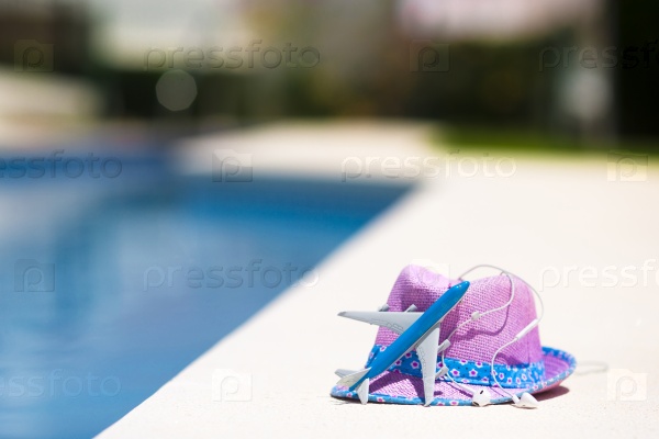 Aircraft model and straw purple hat near swimming pool at summer