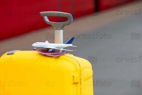 Red passports and airplane small model on yellow luggage at train station