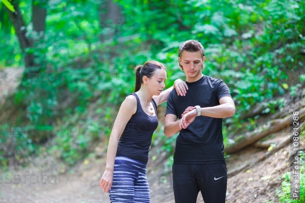 Young active couple looking at smart watch heart rate monitor having break while running at forest