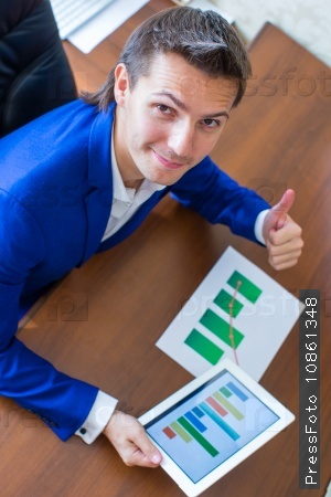 Young businessman working with tablet computer, documents and graphs in his office