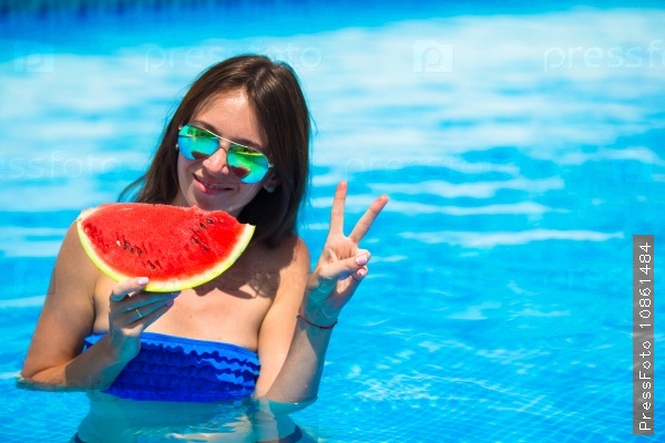 Young woman in hat and sunglasses with watermelon relaxing near swimming pool, stock photo