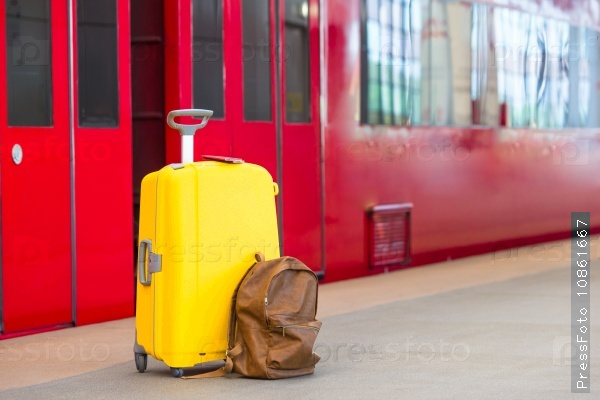 Yellow luggage with passports and brown backpack at train station