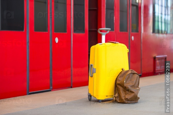 Yellow luggage with passports and brown backpack at train station