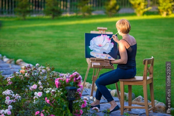 Happy woman painting a picture on an easel on a warm day