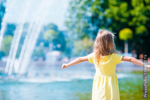 Little happy girl have fun near street fountain at hot sunny day