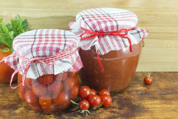Jars of homemade ketchup and cherry tomato next to fresh cherry tomato on wooden background