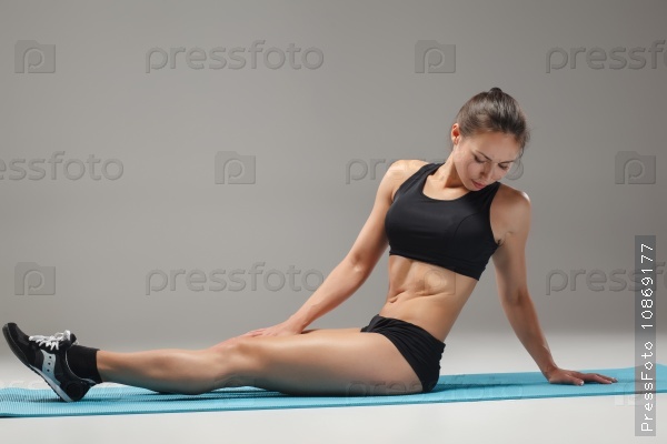 The muscular young woman athlete stretching on gray background, stock photo
