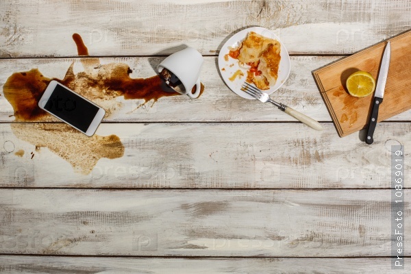 Cup of coffee spilled on wooden table with the phone and and the remnants of a meal, stock photo