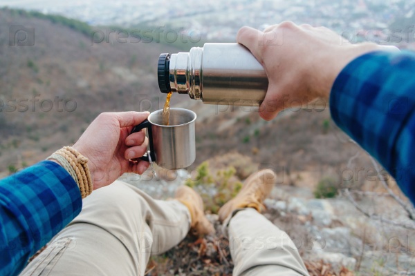 Hiker man sitting in mountains and pouring tea from thermos to cup. Point of view shot, stock photo