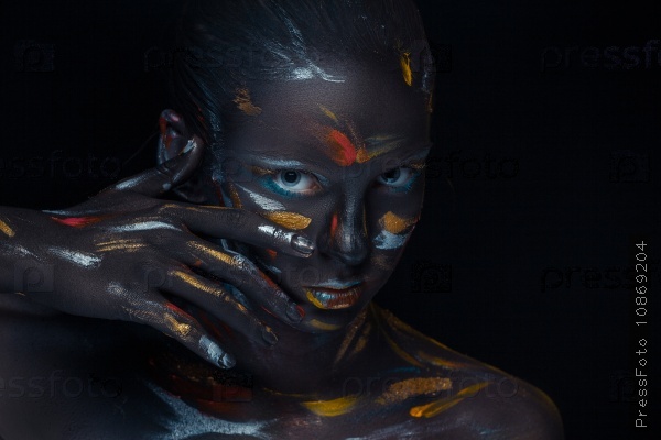 Portrait of a young woman who is posing covered with black paint in the studio on a black background, stock photo