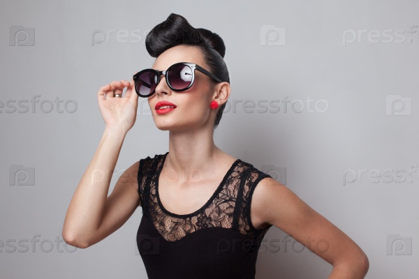 Young fashionable woman in round sunglasses posing in guipure dress. Red lips. Updo, twisted high bun. top knot