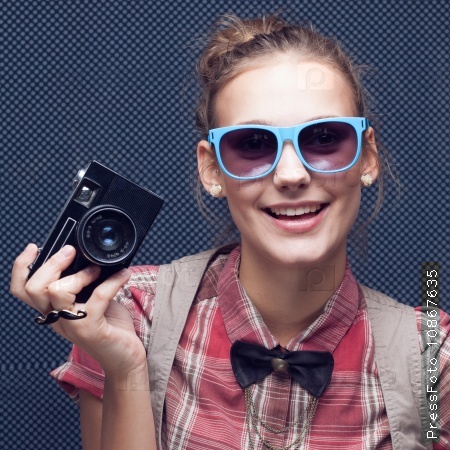 Smiling hipster girl with vintage camera. Trendy teenager in checkered red shirt and bow-tie and sunglasses