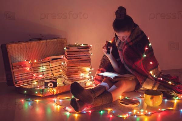 Well-read girl at home in Christmas lights. Night exciting reading by book lover