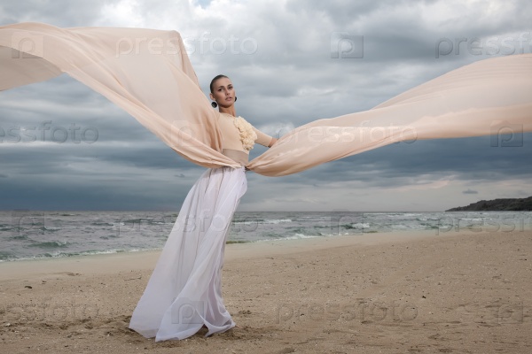 Female model in long beige dress posing dynamic in the beach. waving fabric. fluttering long skirt, stock photo