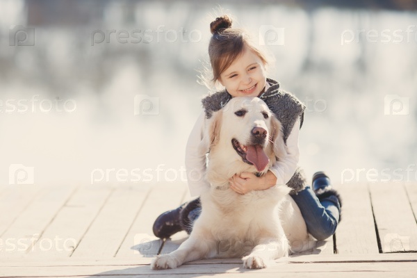 happy little girl with her dog golden retriever sitting on the bridge by the river. Cute little girl hugging golden retriever, smiling. The child with dogs. Puppies and child outdoor.