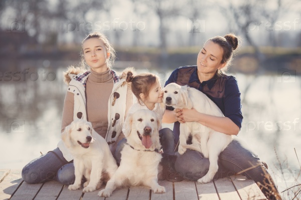 Family Relaxing In Garden With Pet Dogs and puppies. family, pet, animal and people - happy family with labrador retriever dog walking by the river. Happy family playing with their dog on a sunny day
