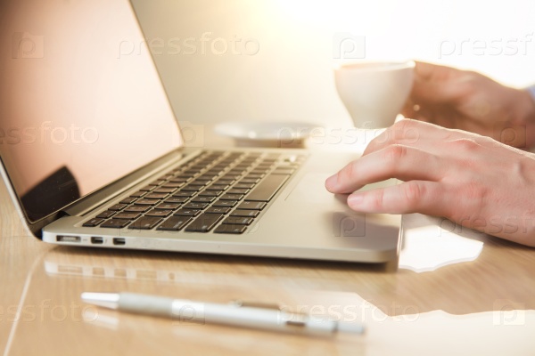 The male hand on the keyboard and hand with coffee on the background of table with pen, stock photo