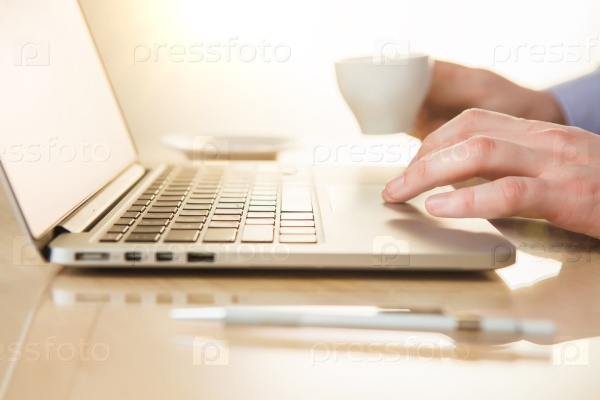 The male hand on the keyboard and hand with coffee on the background of table with pen, stock photo