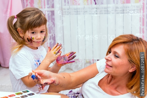 Mom draws paints on a T-shirt daughter lying on the floor. Family fun.