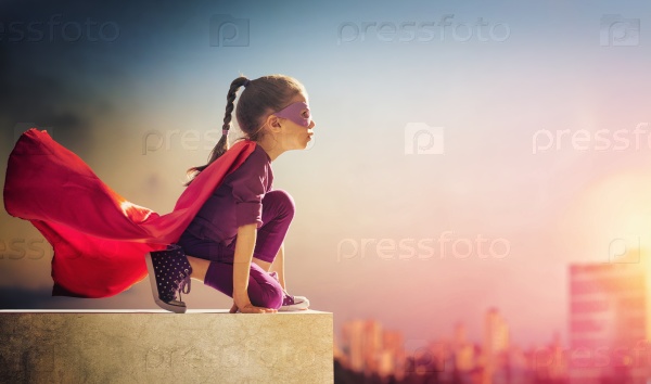 Little child girl plays superhero. Child on the background of sunset sky. Girl power concept