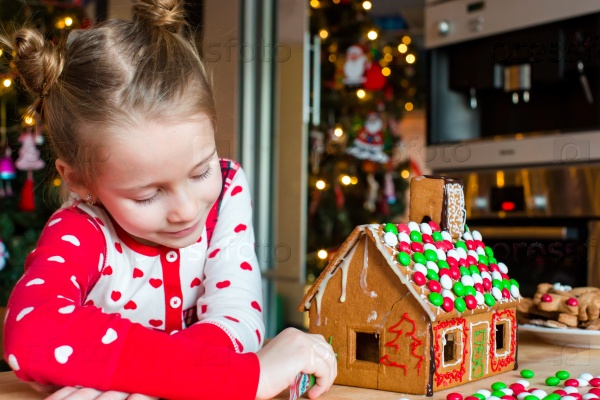 Little adorable girl decorating gingerbread house for Christmas at home, stock photo