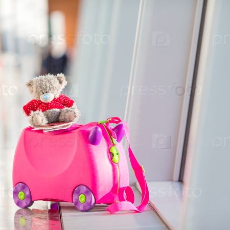 Close up pink small kids suitcase in airport near window, stock photo