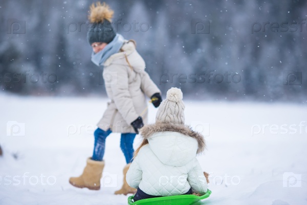 Little adorable girls enjoy a sleigh ride. Child sledding. Children play outdoors in snow. Family vacation on Christmas eve outdoors, stock photo