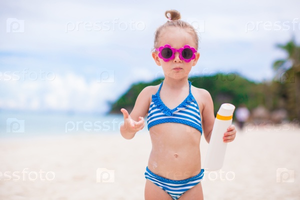 Little adorable girl with suntan lotion bottle on white beach, stock photo