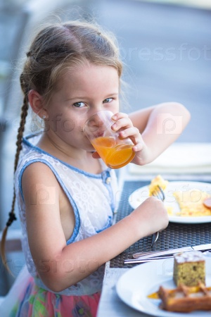 Adorable little girl drinking apple juice for breakfast in outdoor cafe