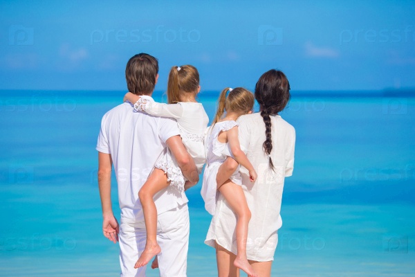 Back view of young family of four on white beach during summer vacation