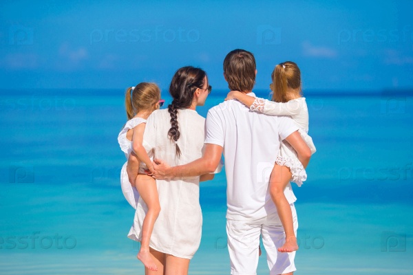 Back view of young beautiful family on white tropical beach