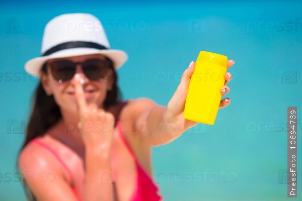 Young happy woman applying suntan lotion on her nose on white beach