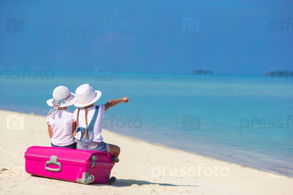 Little adorable girls with big suitcase on tropical white beach during summer vacation