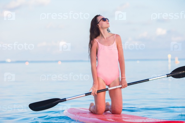 Beautiful young woman surfing on stand up paddle board at exotic vacation, stock photo