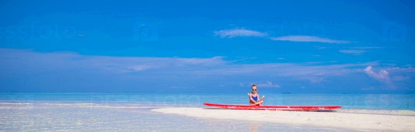 Little girl in yoga position on surfboard at tropical beach