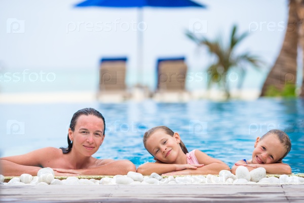 Mother and two little kids enjoying summer vacation in luxury swimming pool
