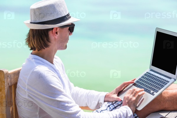 Young man with tablet computer and cell phone on tropical beach, stock photo