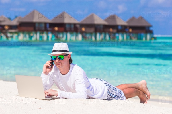 Young man working on laptop at tropical beach near water villa, stock photo