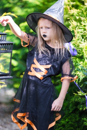 Adorable amasing little girl wearing witch costume on Halloween outdoors. Trick or treat.