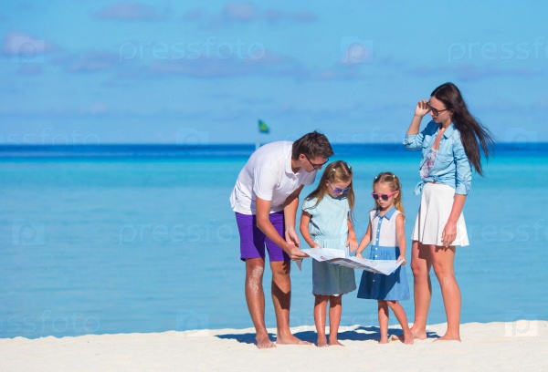 Happy young family of four with map on the beach