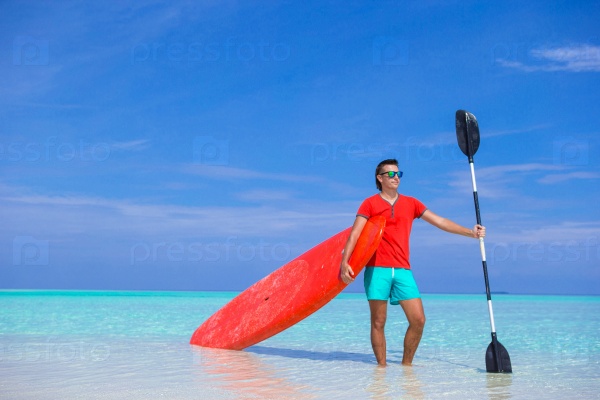 Happy young man with surfboard and paddle on the tropical coast