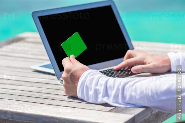 Closeup of green credit card and computer on table background the sea, stock photo