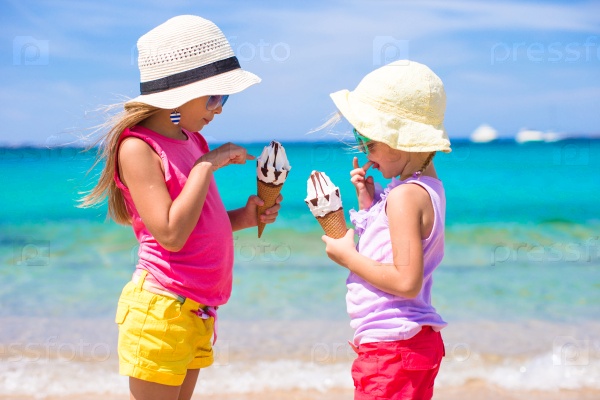 Happy little girls eating ice-cream over summer beach background. People, children, friends and friendship concept