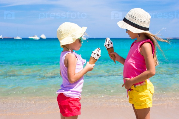 Happy little girls eating ice-cream over summer beach background. People, children, friends and friendship concept, stock photo